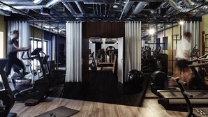 Un gimnasio moderno con equipo de ejercicio, suelo de madera y conductos expuestos.