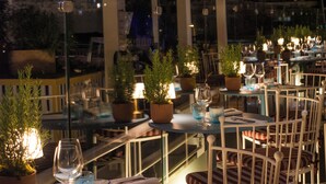 Un restaurante con mesas redondas, sillas, plantas en macetas y cristalería.