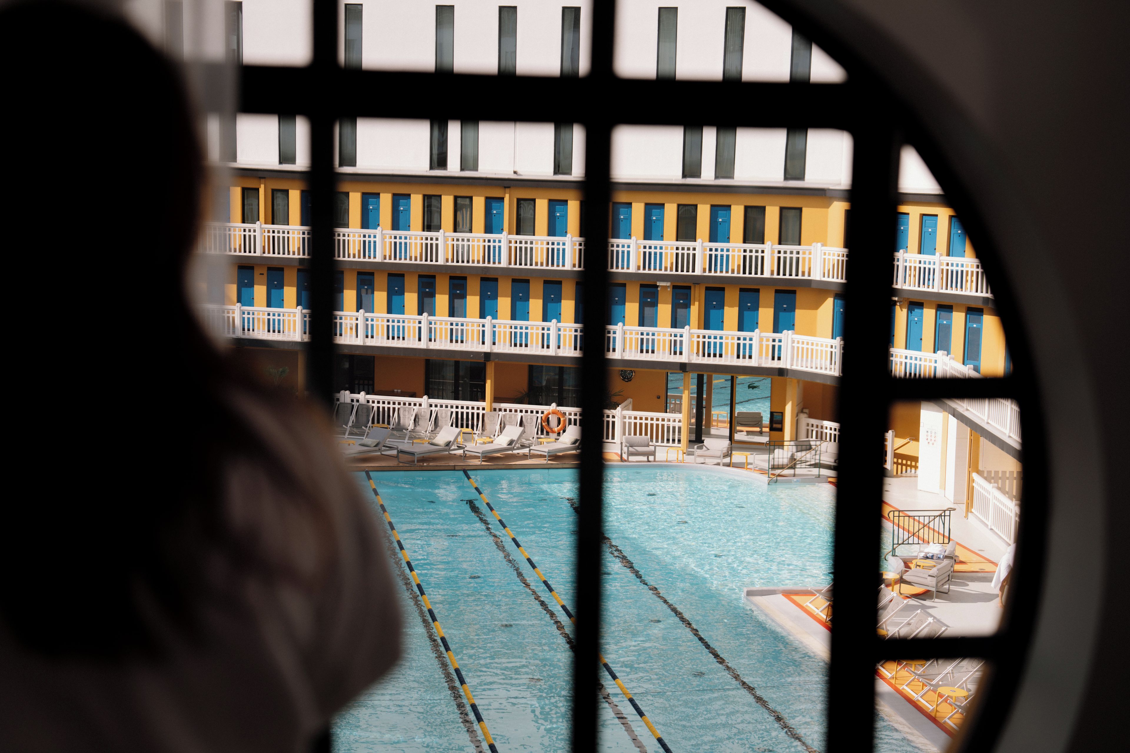 A swimming pool with multiple lanes, a building with balconies, and a view through a window.