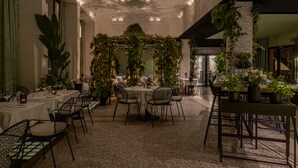 Un restaurante con mesas redondas, sillas negras y un arco central con follaje.