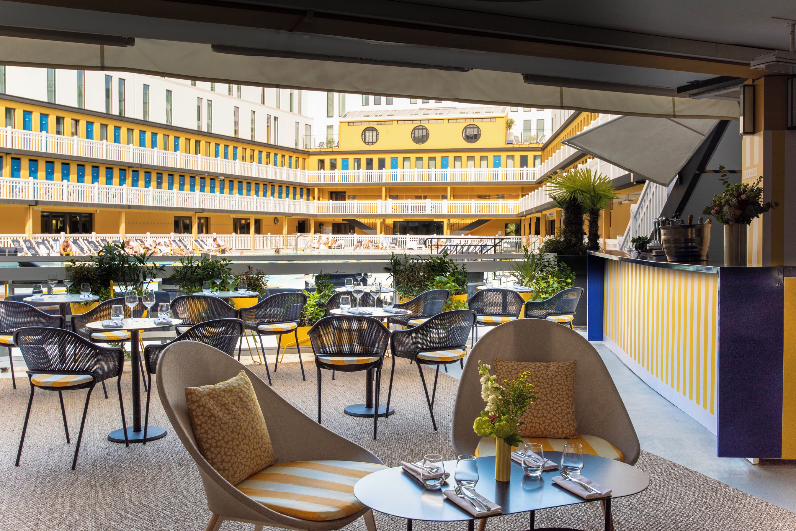 Un espace extérieur aménagé avec des tables et des chaises, offrant une vue sur un immeuble jaune doté de nombreux balcons.