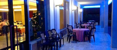 Zona de menjador interior amb taules i cadires, un separador de vidre i vista a una sala de dinar.
