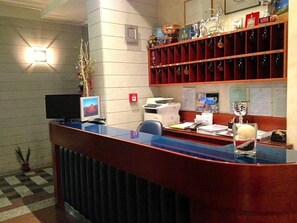 A reception desk with a computer, printer, and various items on shelves.