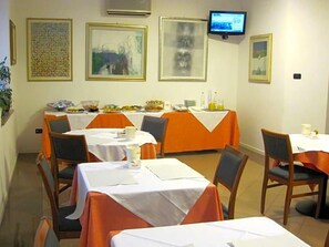 Un espace repas avec des tables dressées pour les repas, un téléviseur fixé au mur et des œuvres d’art encadrées qui décorent les murs.