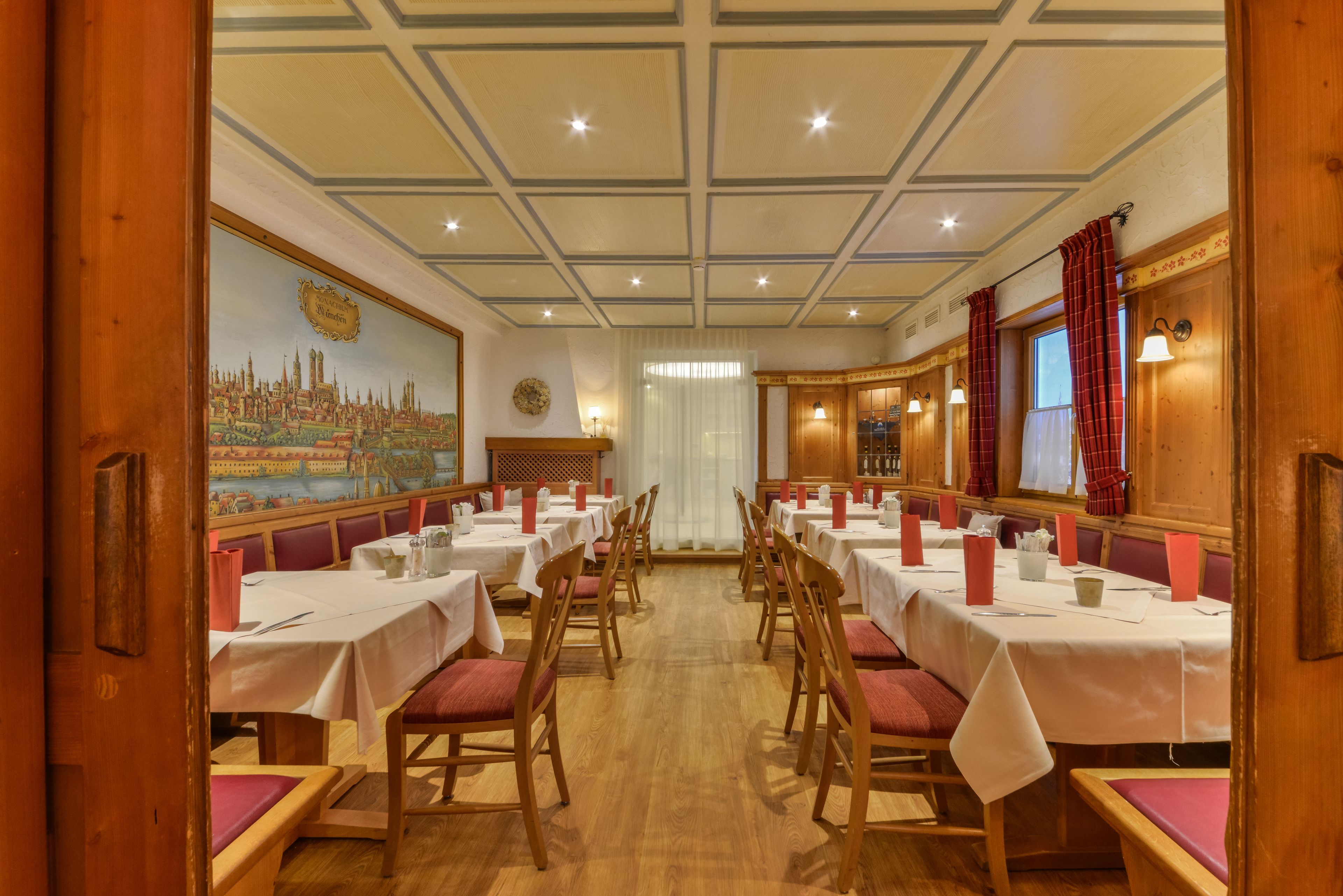 Uma sala de jantar com mesas compridas, cadeiras de madeira e um mural na parede.