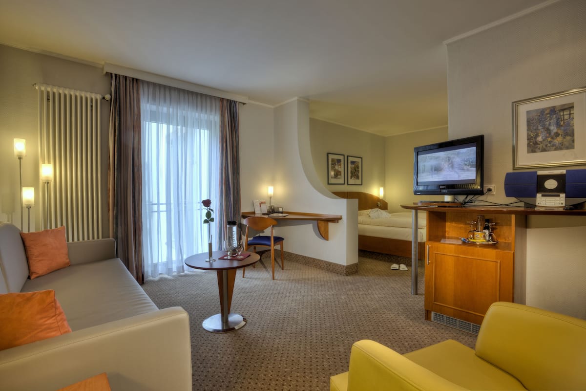 A hotel room with a sofa, a small table, a desk, a television, and a cabinet.