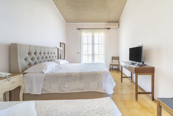 Un dormitorio con dos camas, un escritorio y televisión, y una ventana con cortinas.