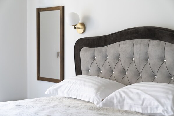 Una cama bien hecha con cabecera acolchada, una lámpara de pared y un espejo.