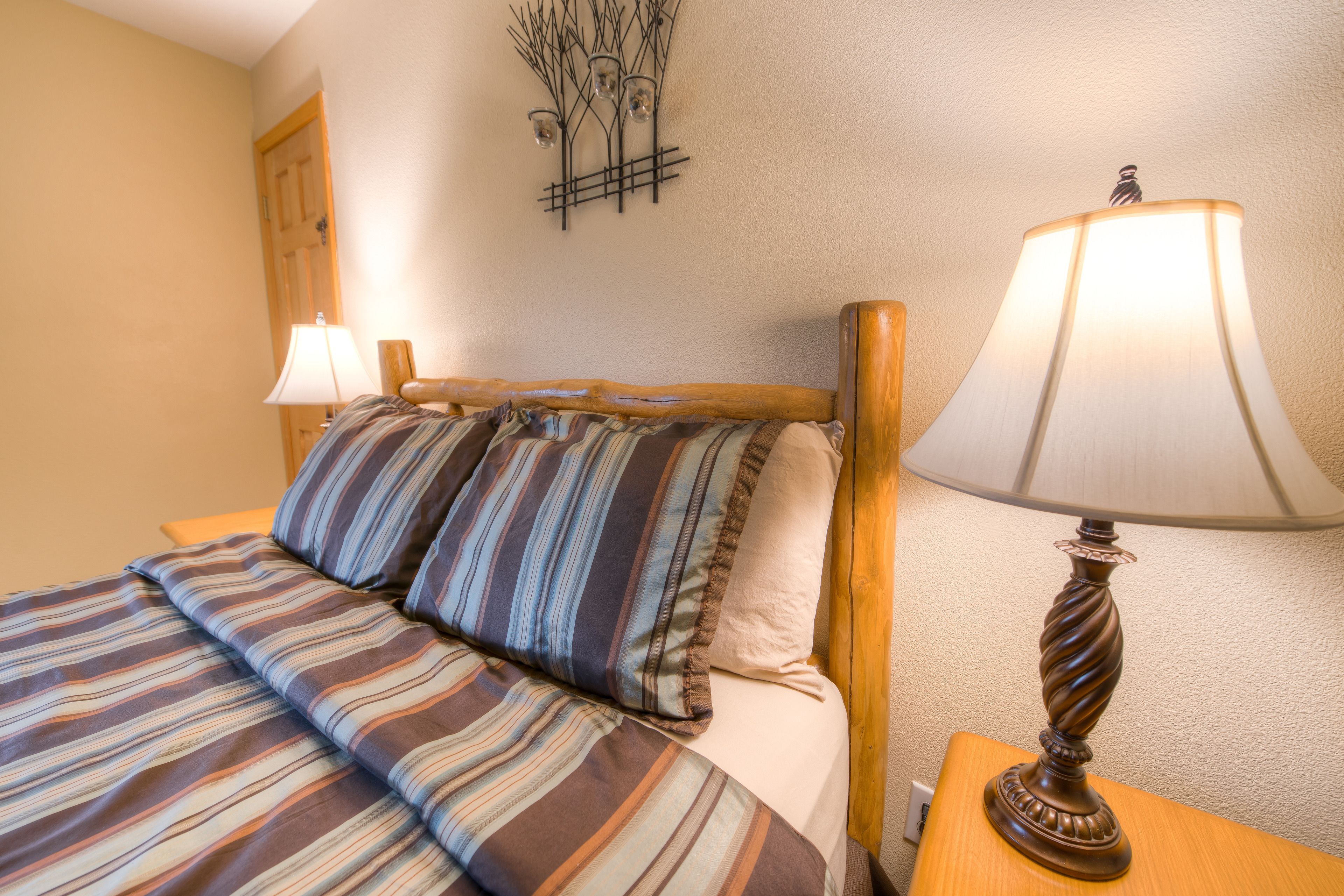 Uma cama bem arrumada com roupa de cama listrada, uma cabeceira de madeira e uma mesa de cabeceira com abajur.