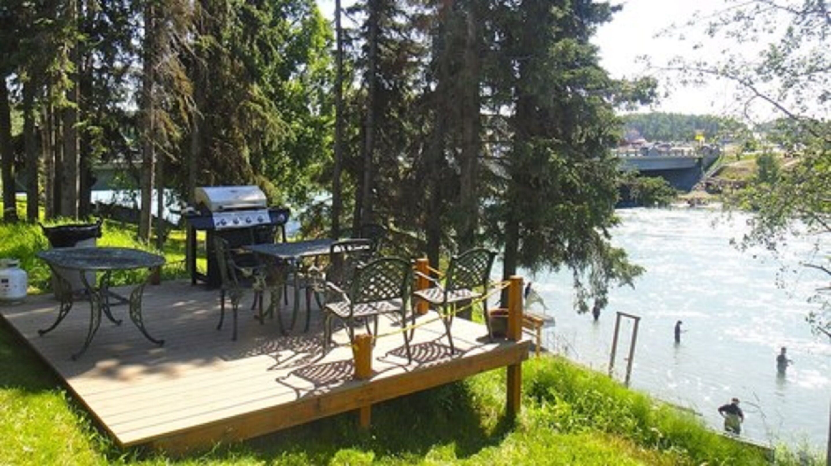 An outdoor deck with a grill, tables, and chairs overlooking a river.
