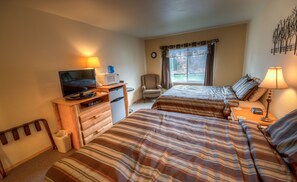 A hotel room with two beds, a television, a desk with a computer, a chair, and a window with curtains.