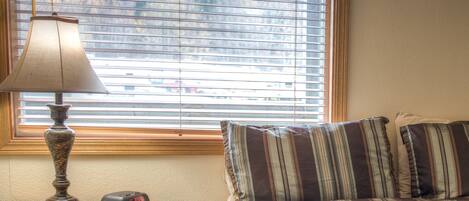 A bedroom with a bed, a bedside table with a lamp, and a window with blinds.