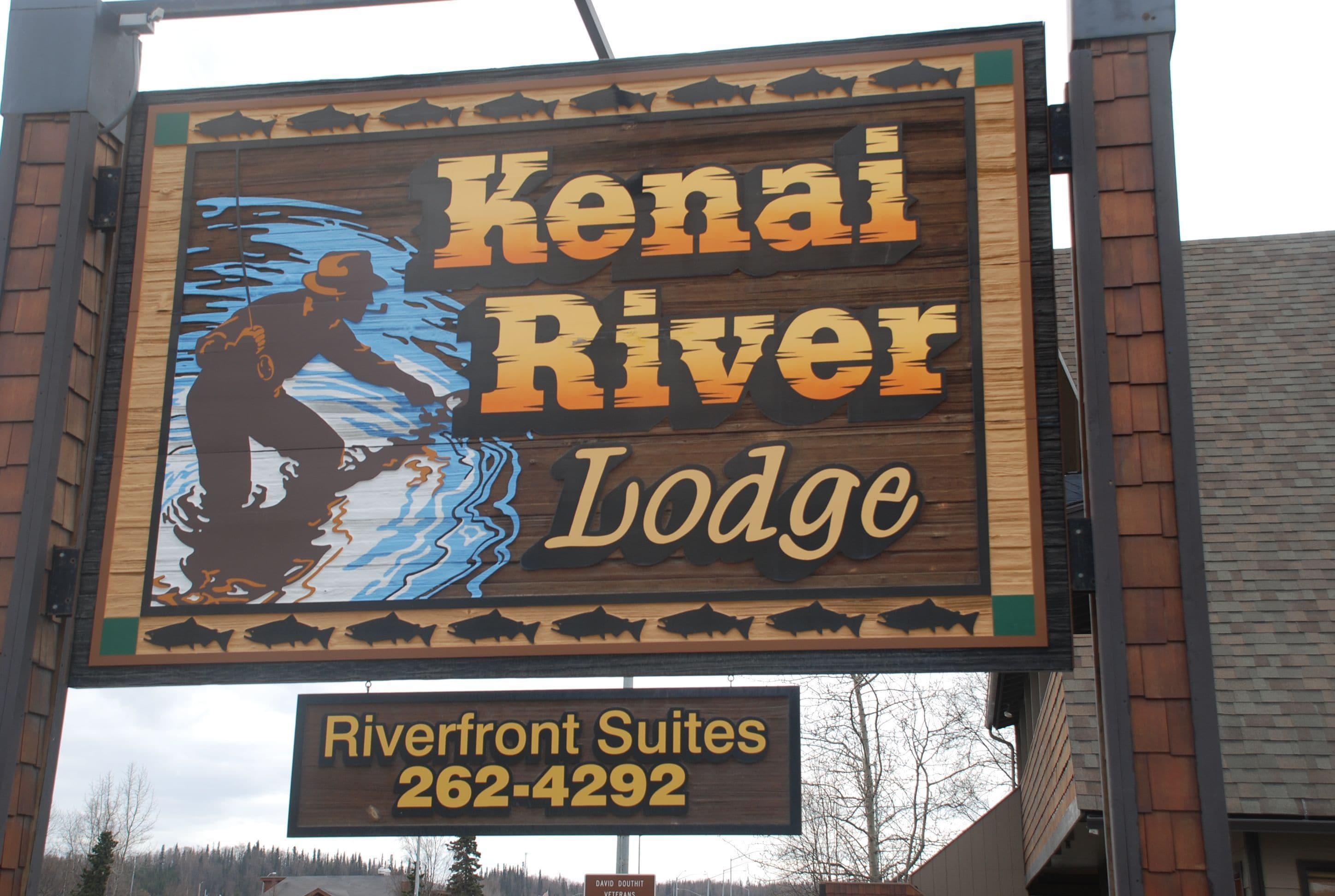 Une enseigne pour le Kenai River Lodge, représentant en silhouette une personne en train de pêcher. Elle indique le nom du lodge et un numéro de téléphone pour Riverfront Suites.