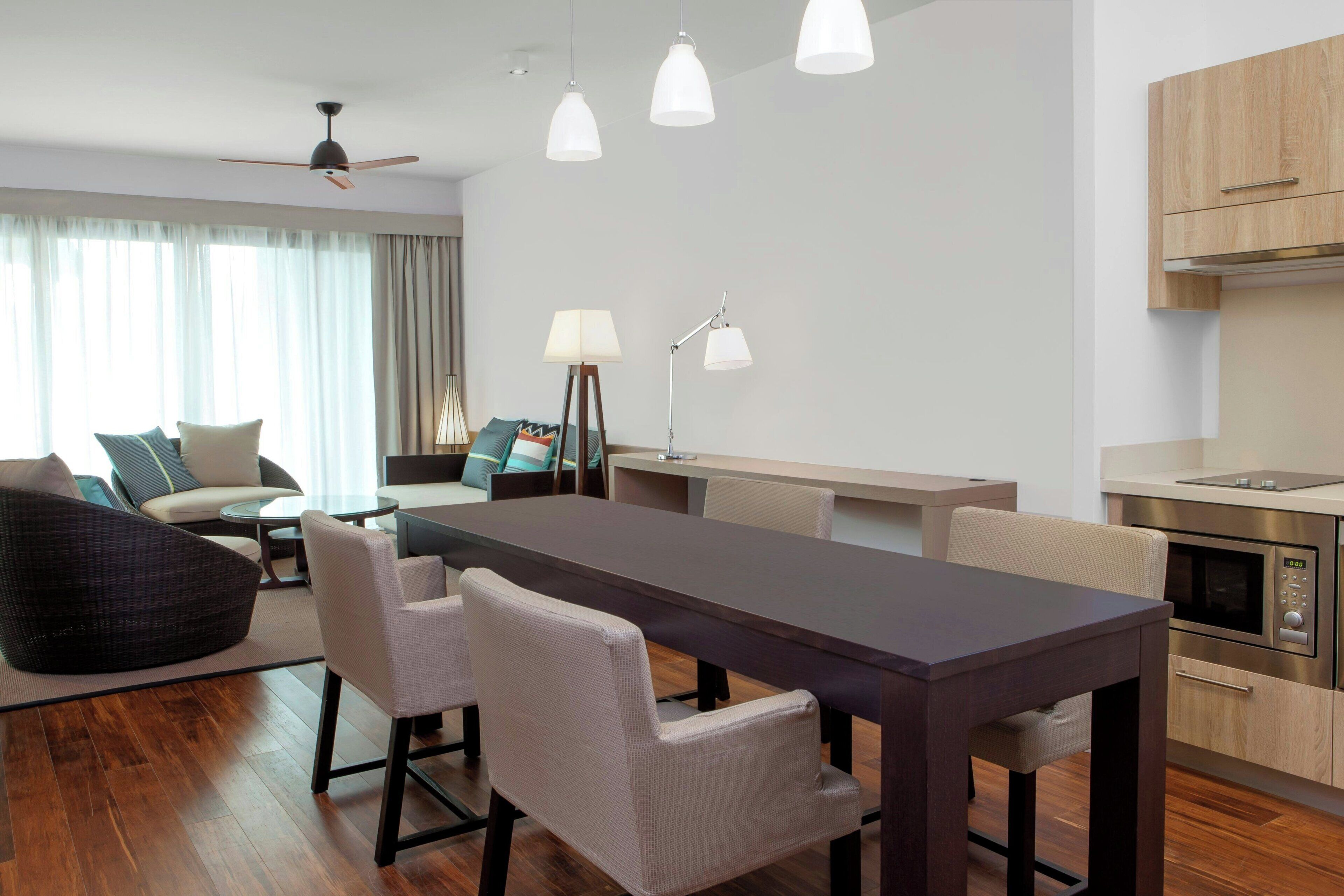 Een moderne woonkamer met een eettafel, stoelen, een bank en een keukenhoek met een magnetron.