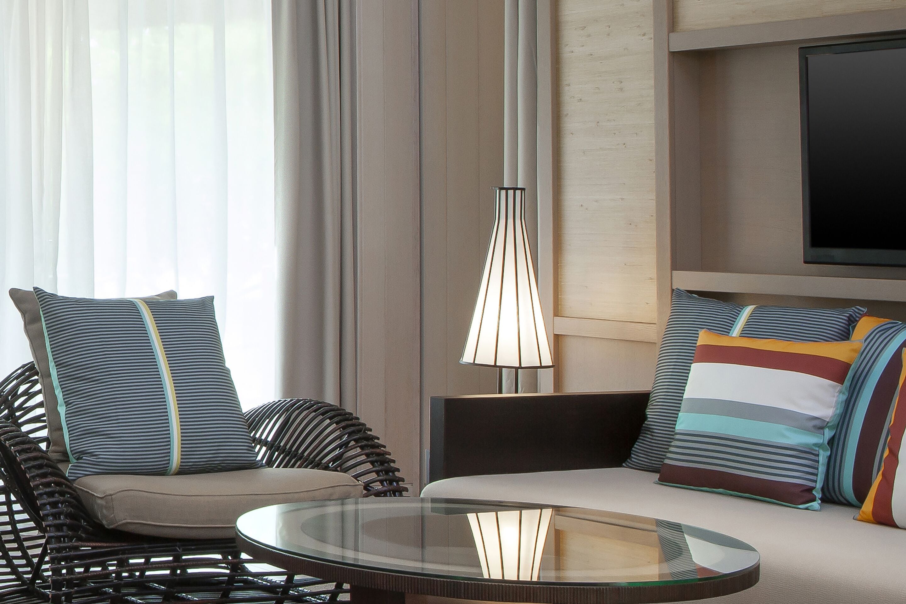 A modern living room with a glass coffee table, striped cushions, and a hanging light fixture.