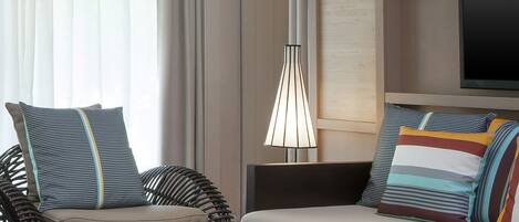 A modern living room with a glass coffee table, striped cushions, and a hanging light fixture.