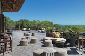A wooden deck with outdoor seating, including sofas and ottomans, overlooking a body of water. - Le Domaine Déva, Series by Marriott (Bourail)