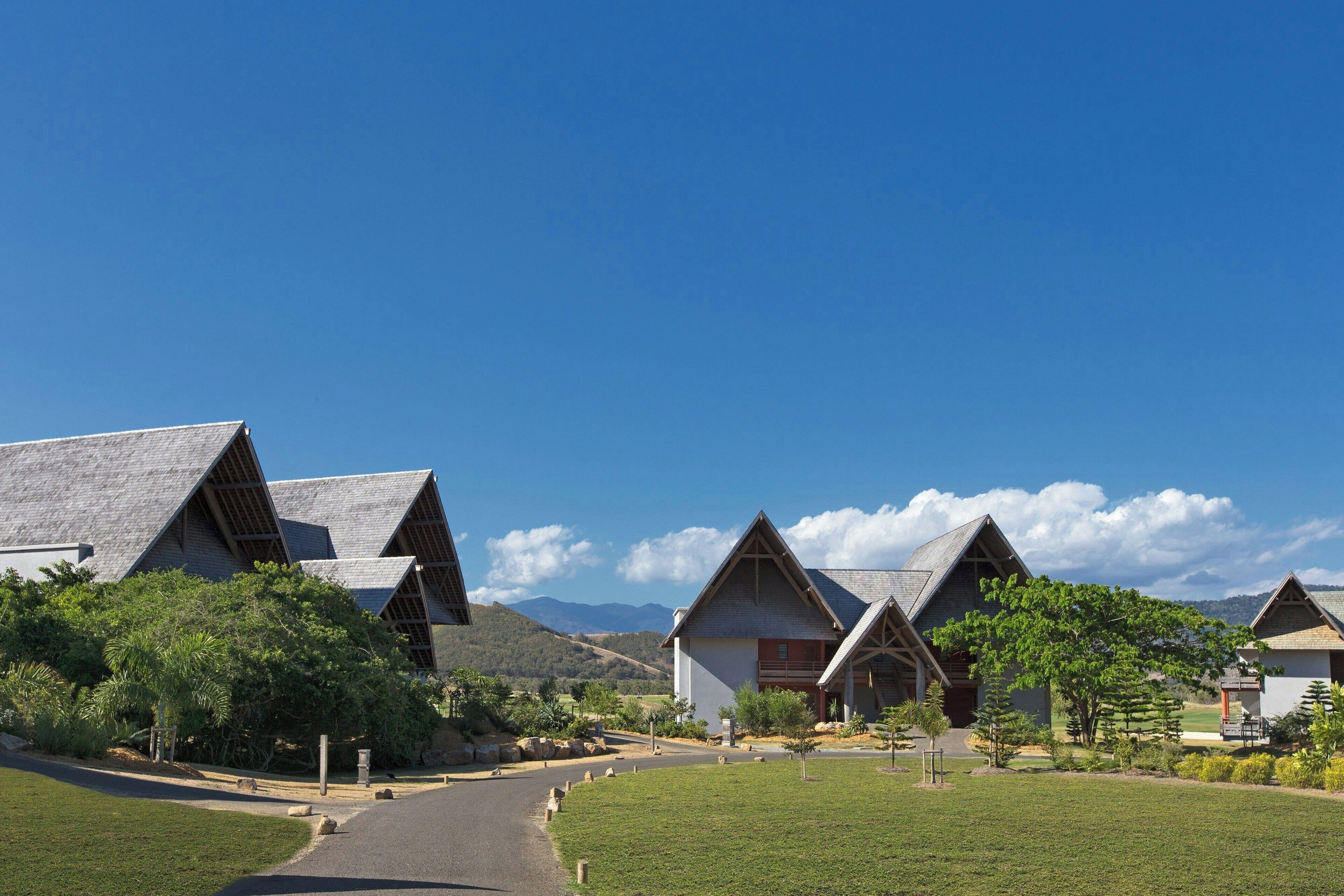 A row of triangular-roofed buildings with a clear sky and distant mountains.