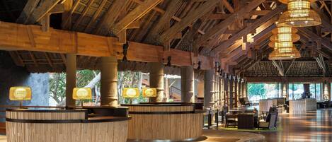 A spacious lobby with wooden reception desks, hanging lamps, and a high ceiling with exposed beams.