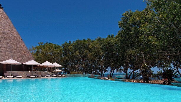 A clear blue pool with lounge chairs and umbrellas, surrounded by trees and a large rock formation. - Le Domaine Deva, Series by Marriott (Bourail)