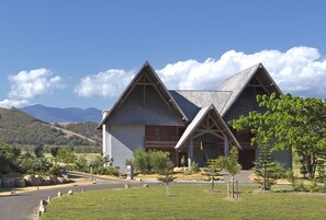 A modern building with a triangular roof and a stone facade, surrounded by a well-maintained lawn and trees. - Le Domaine Déva, Series by Marriott (Bourail)