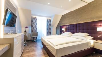 A modern hotel room with a large bed, a TV mounted on the wall, a desk with a chair, and a window with curtains.