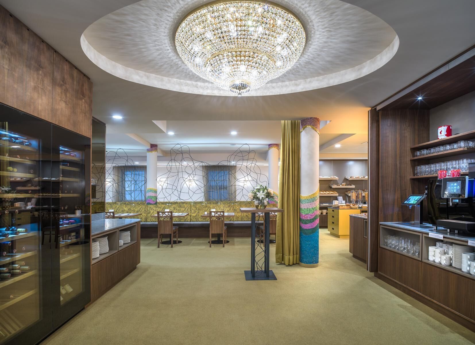 A hotel lobby with a central seating area, a chandelier, and a reception desk.