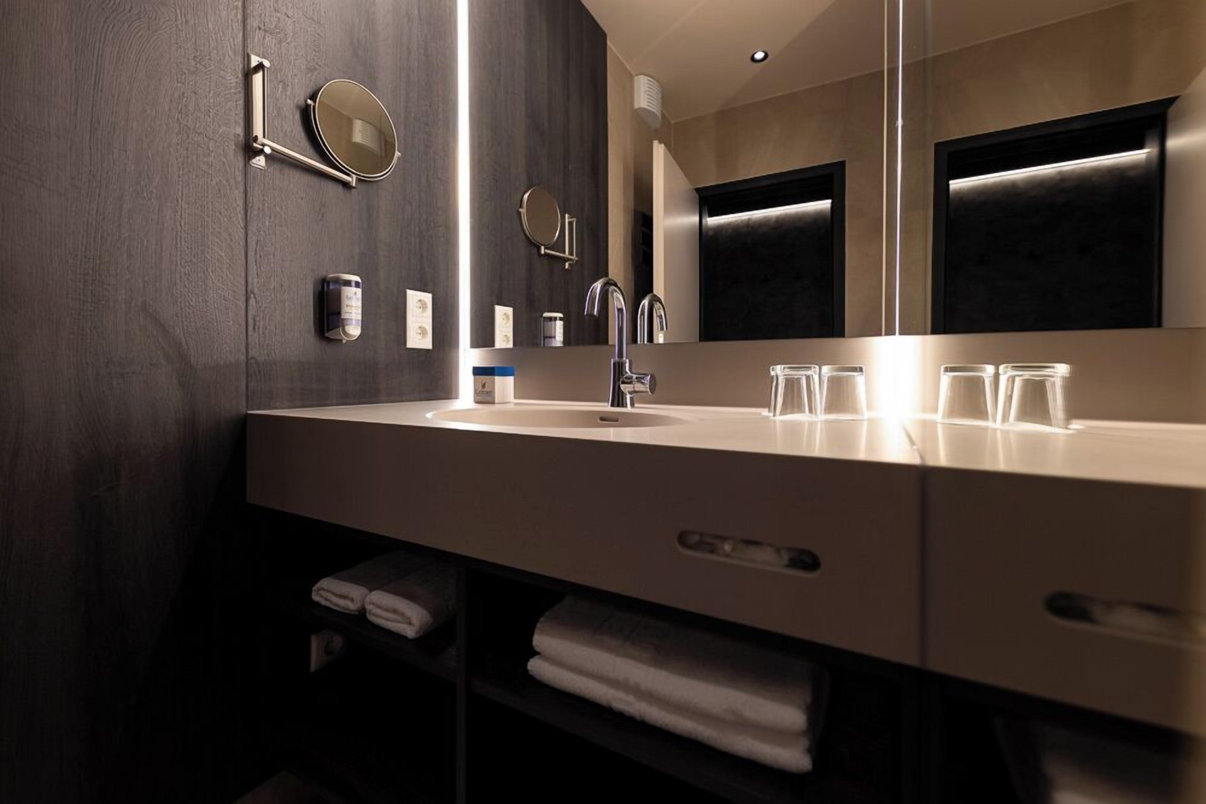 Un baño moderno con un espejo grande, un lavamanos y un perchero para toallas.
