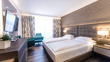 A modern hotel room with a large bed, a desk, a chair, and a TV.