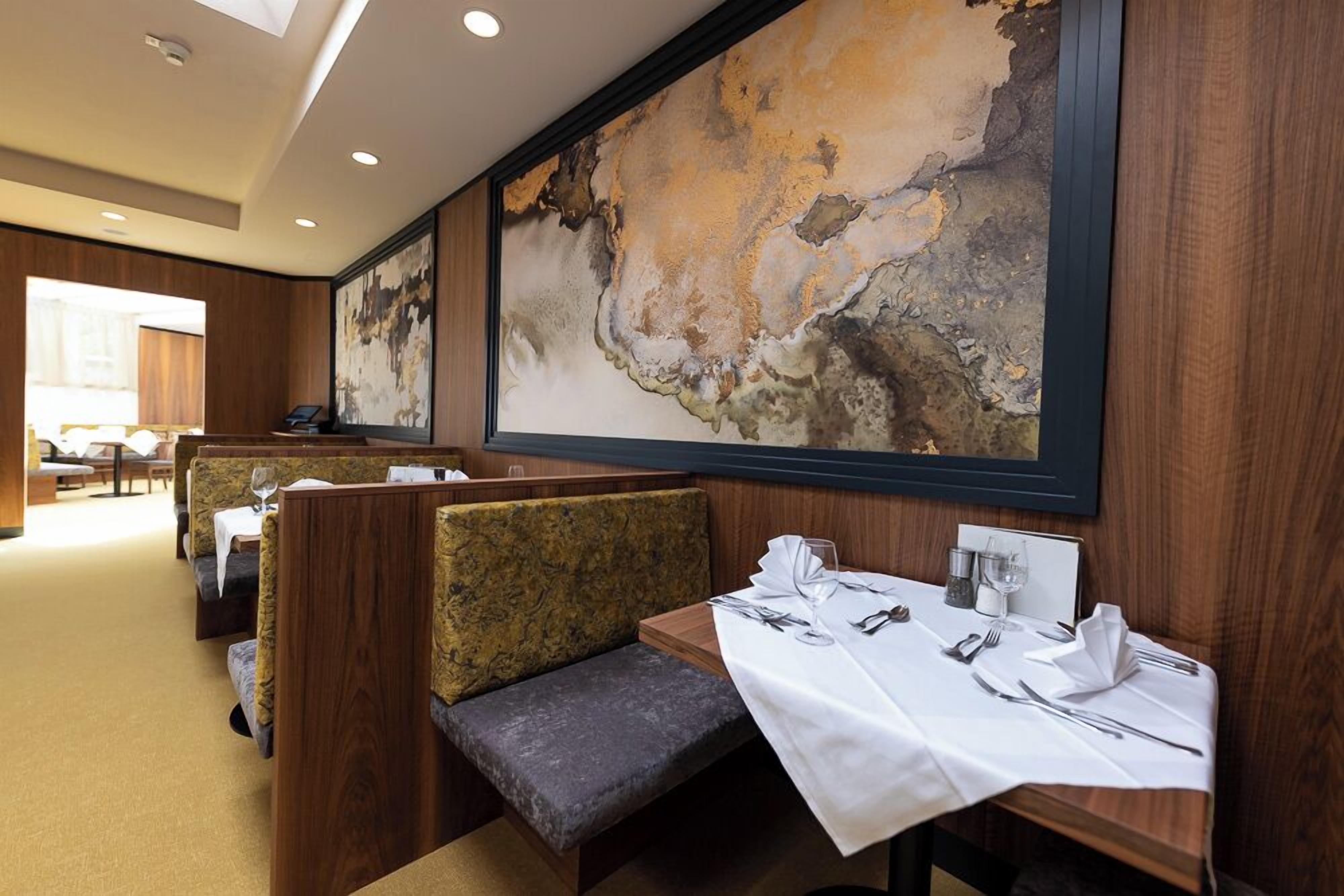 Un restaurante con asientos tipo cabina, un mantel blanco y un cuadro abstracto grande en la pared.