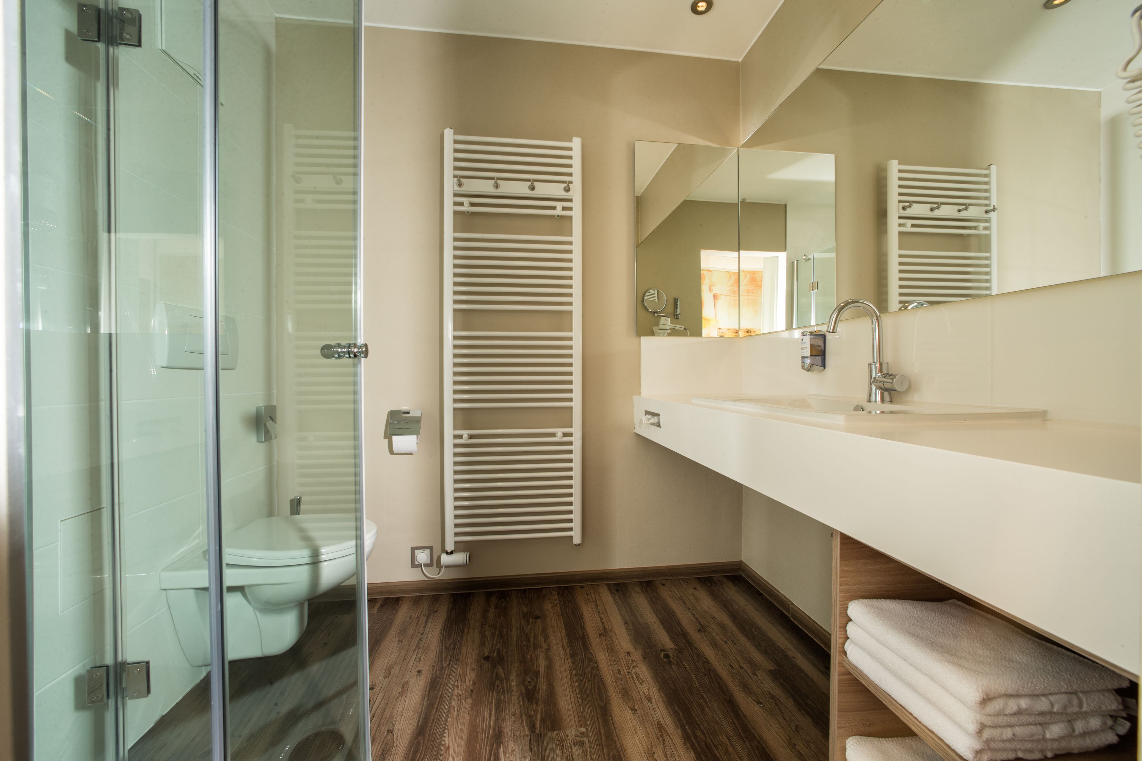 Un baño moderno con cabina de ducha de vidrio, inodoro, toallero blanco y espejo sobre el lavamanos.