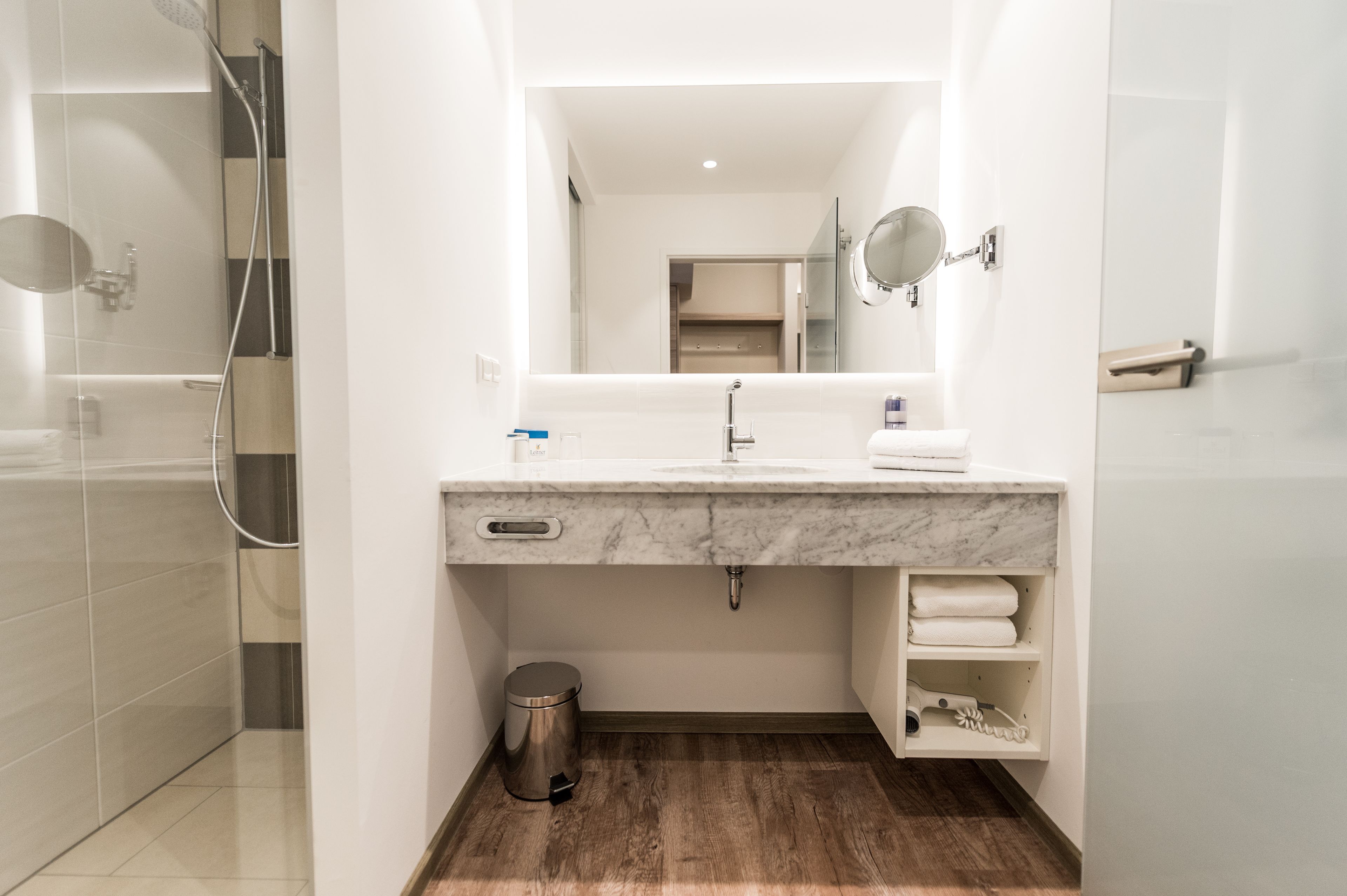 Un baño moderno con lavamanos de mármol, un espejo, toallero y zona de ducha.