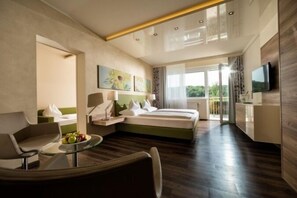 A modern hotel room with a bed, a seating area with a table, a TV, and a balcony with a view. - Thermalhotel Leitner (Loipersdorf bei Fuerstenfeld)