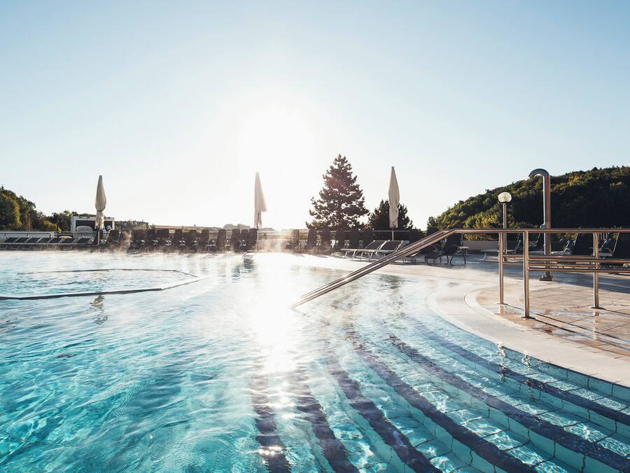 A swimming pool with clear water, sun, and trees in the background.