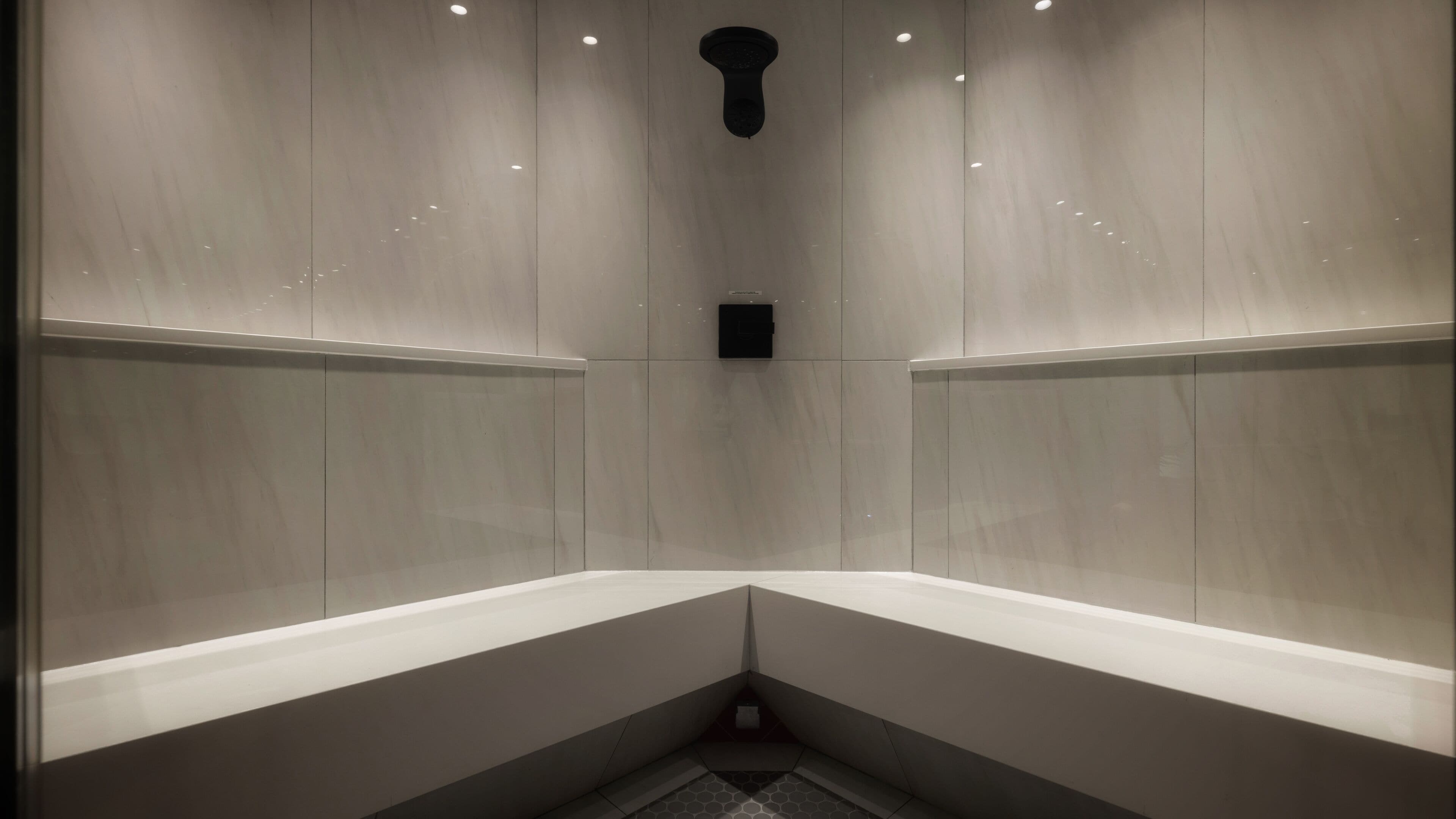 Un baño moderno y minimalista con ducha en esquina, paredes con azulejos e iluminación empotrada.