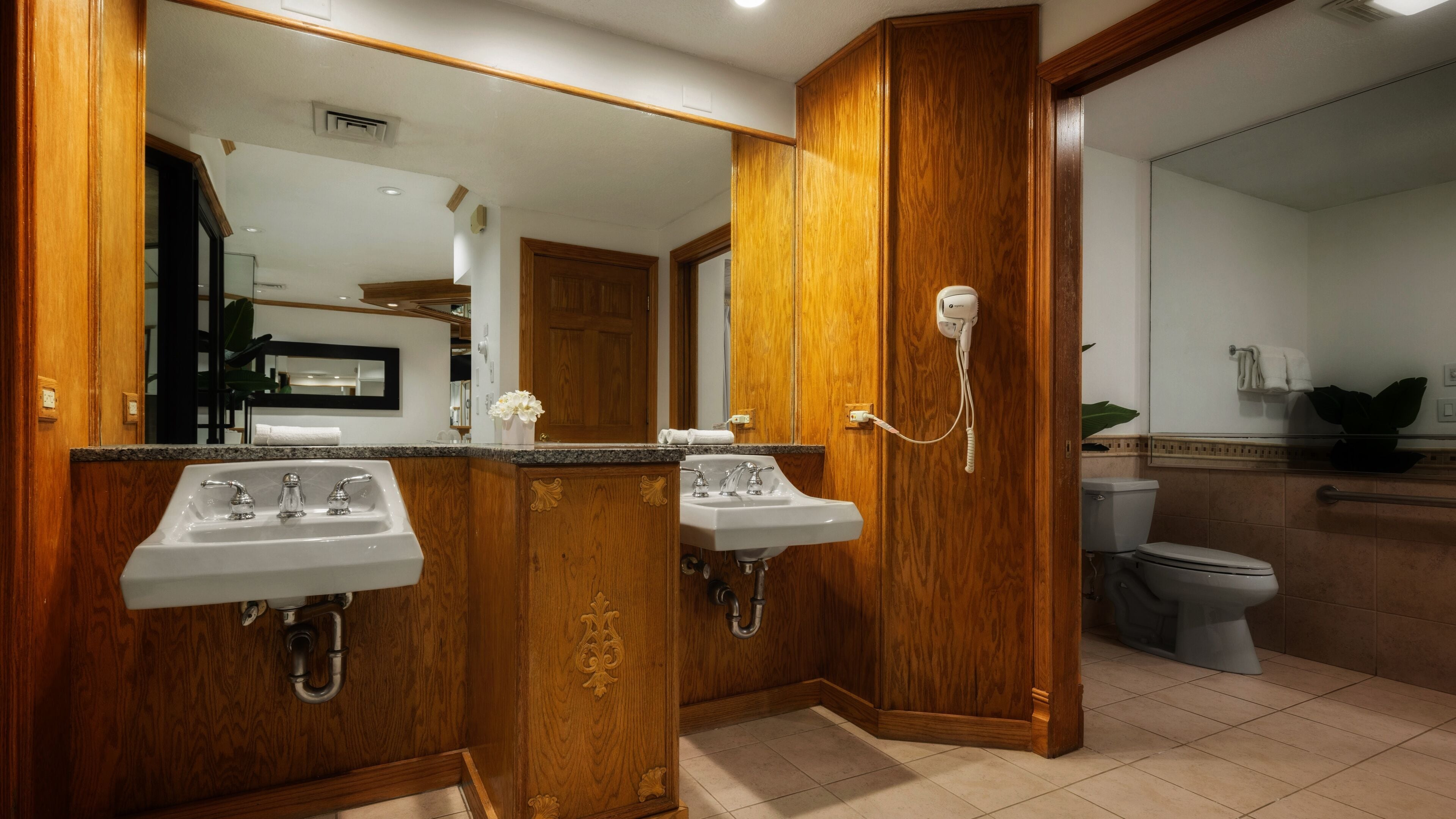 A bathroom with two sinks, wooden cabinetry, a mirror, and a toilet.