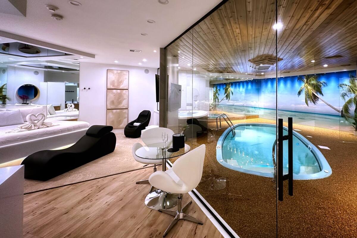 A modern hotel room with a glass-enclosed infinity pool, a wooden ceiling, and a beach-themed mural.