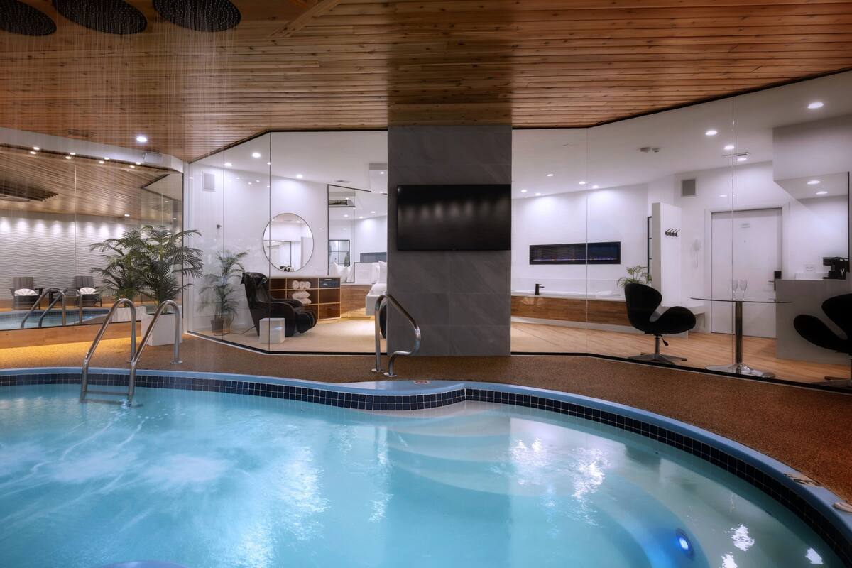 A modern indoor pool area with a clear view of the adjacent spa room, a reception desk, and seating area.