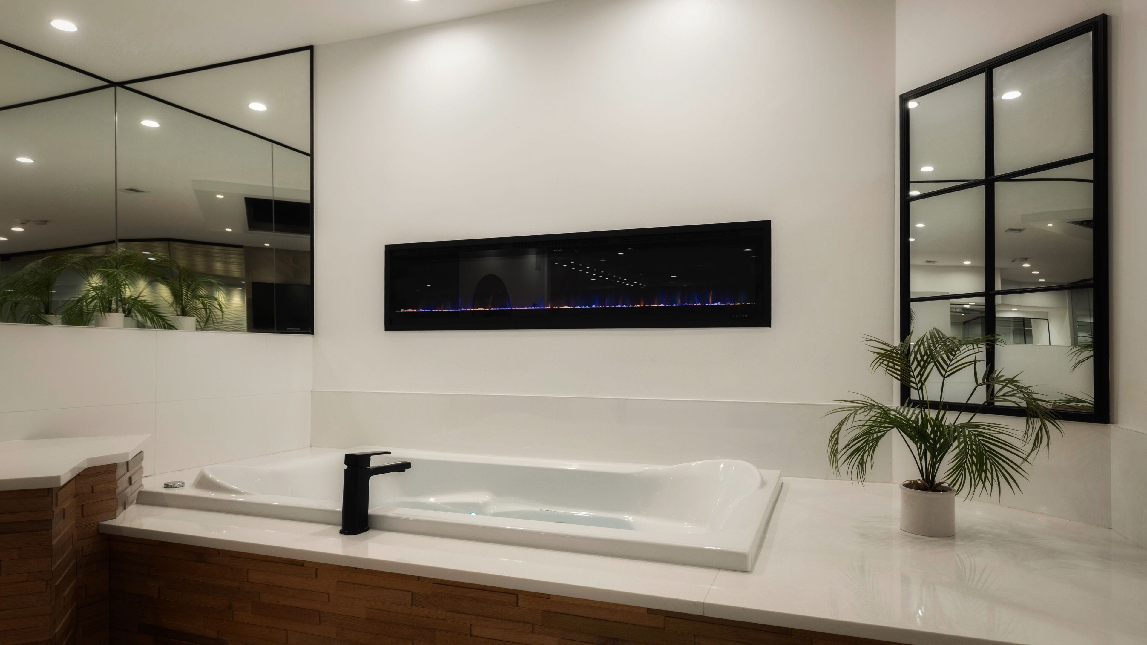 Un baño moderno con una bañera amplia, un espejo y un televisor empotrado que muestra un paisaje urbano nocturno.