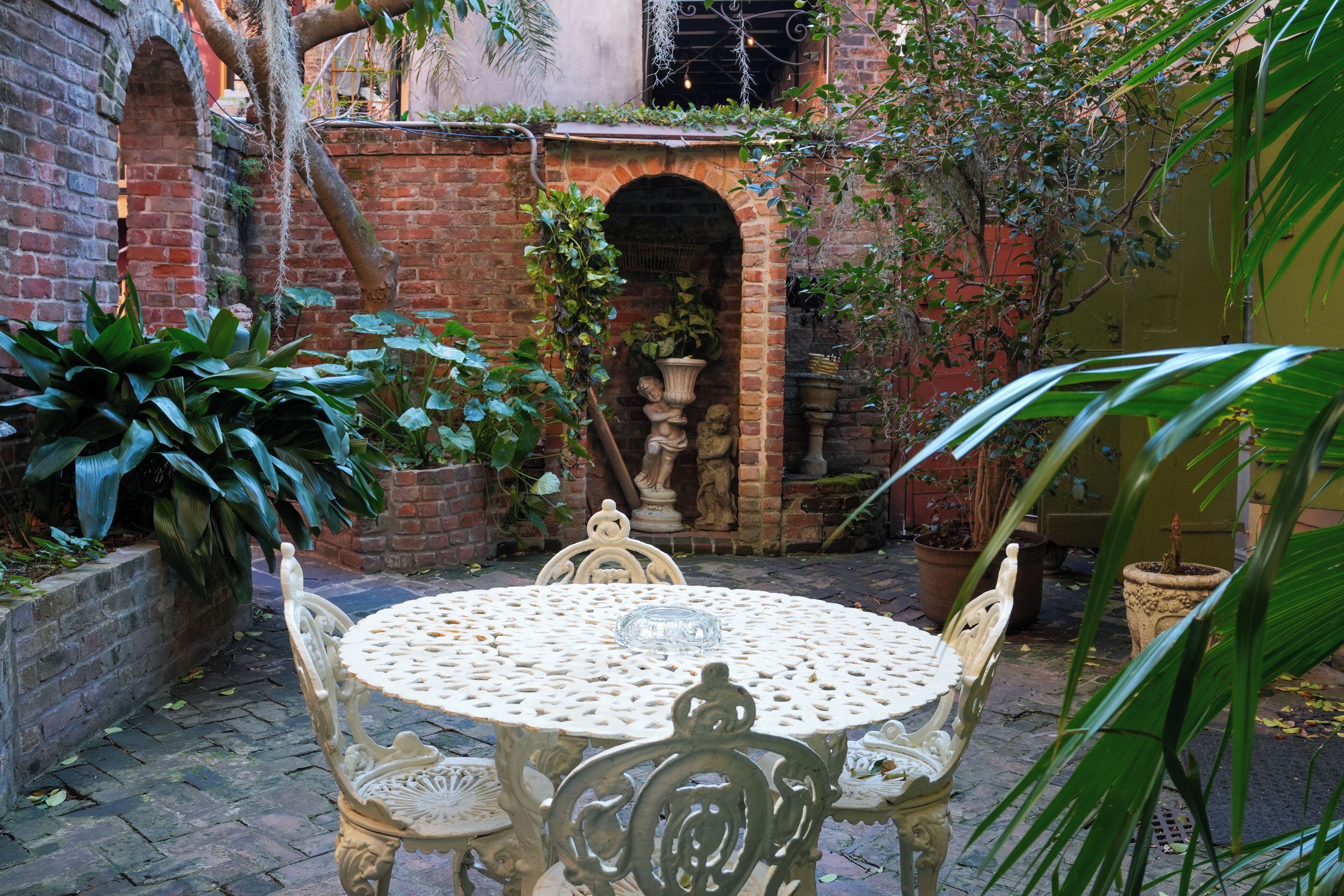 A courtyard with a round table and chairs, surrounded by potted plants and a brick wall.