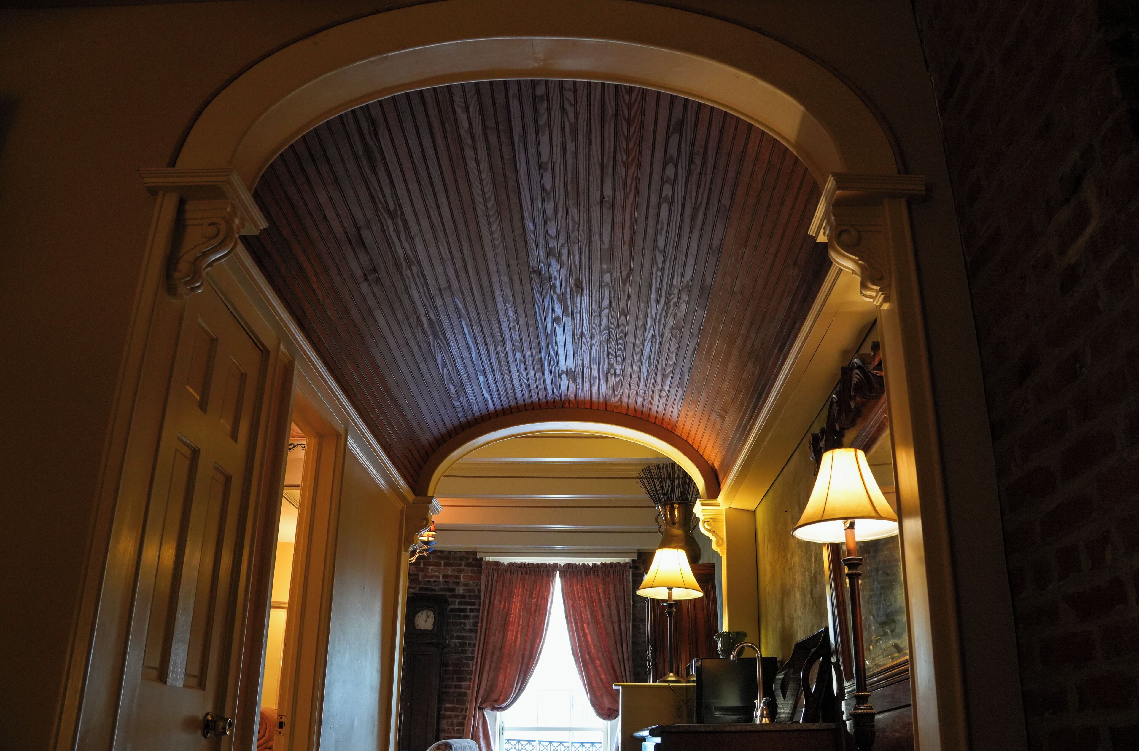 Un pasillo abovedado con techo de madera, una puerta, una ventana con cortinas y una lámpara.
