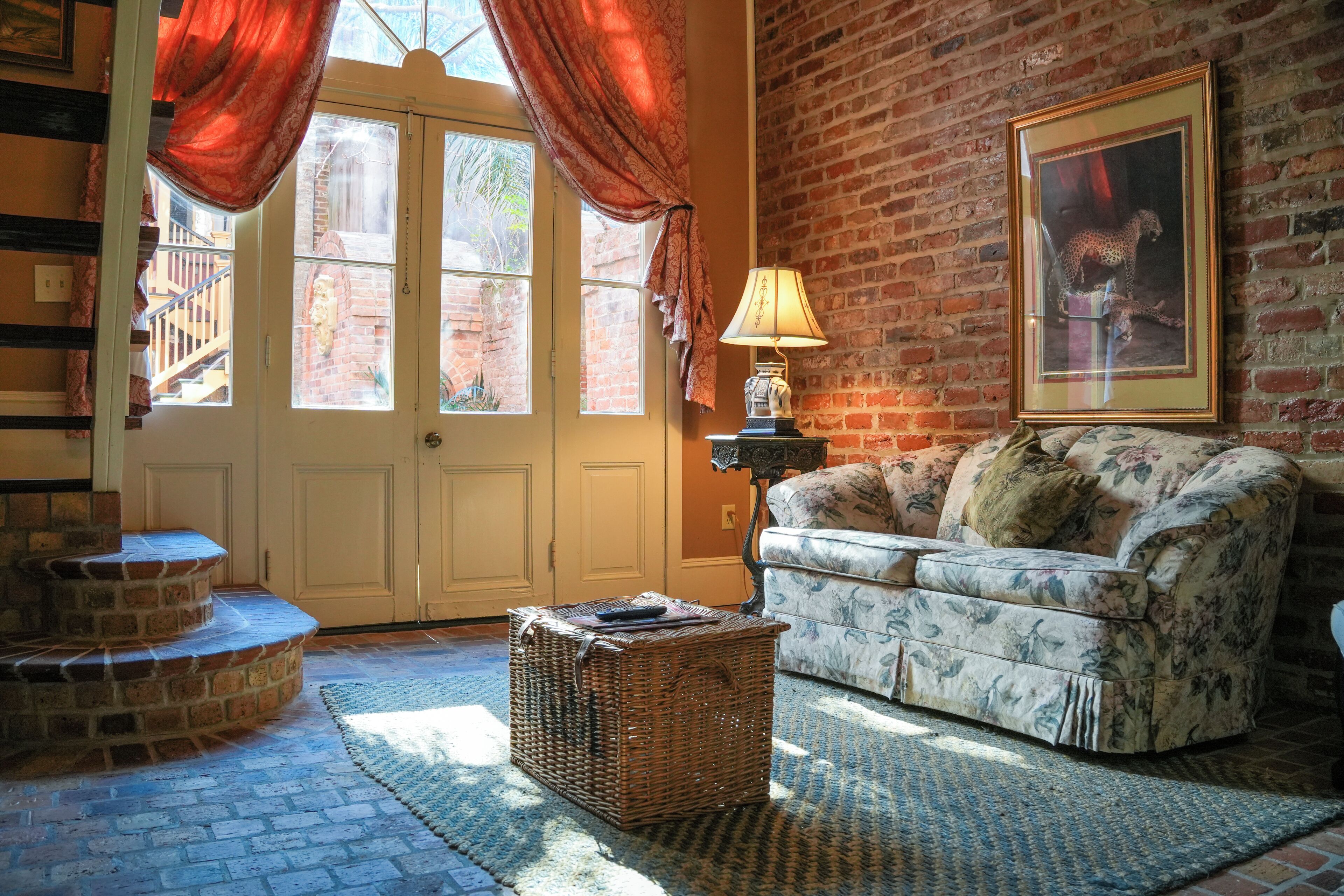 A living room with a brick wall, a sofa, a lamp, a basket, and a door with curtains.