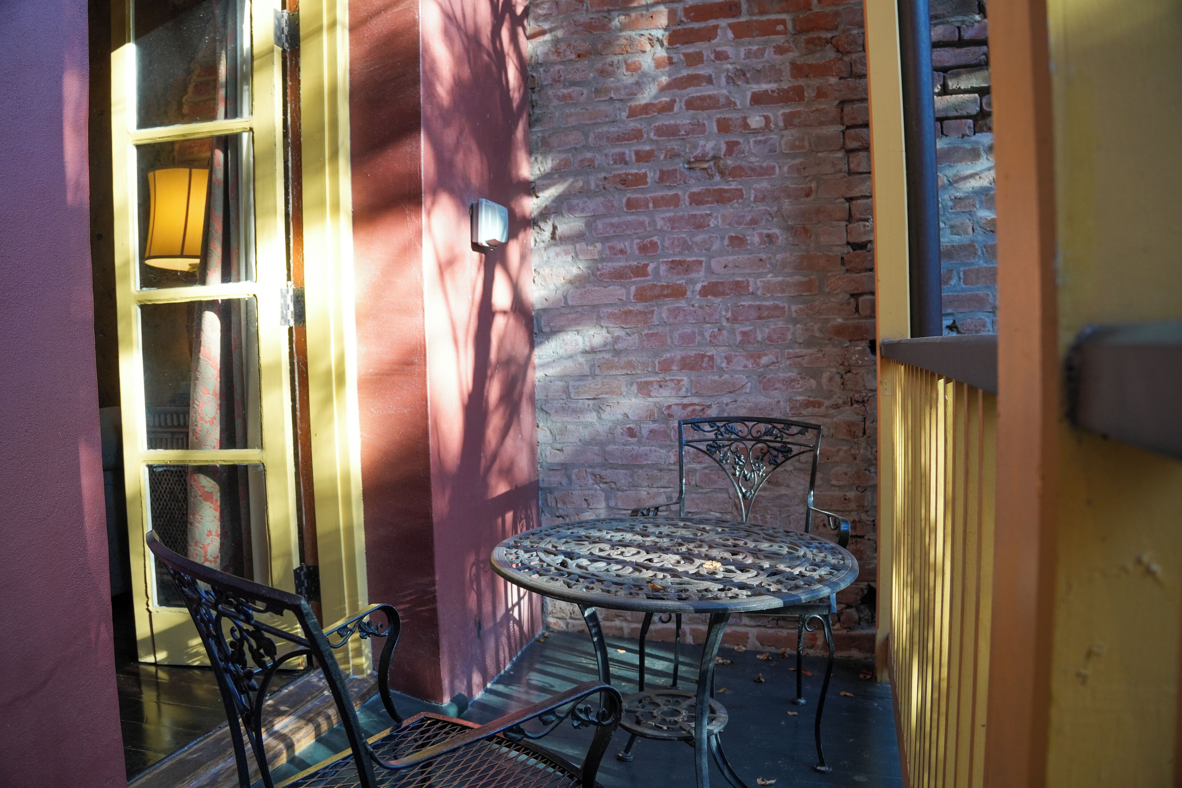 A small outdoor patio with a metal table and chairs, a brick wall, and a door with a glass panel.