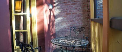 A small outdoor patio with a metal table and chairs, a brick wall, and a door with a glass panel.