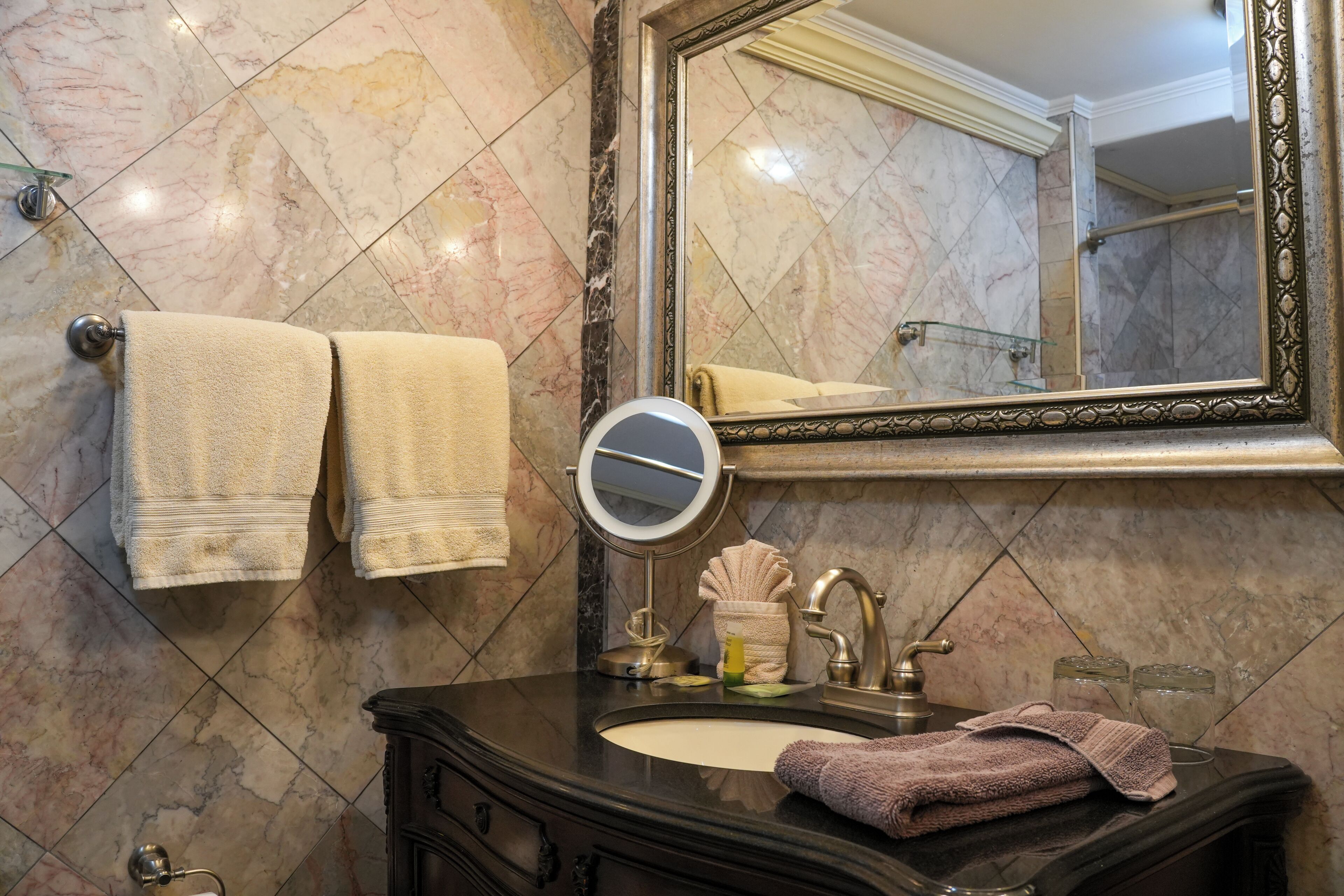 A bathroom with a marble-tiled wall, a round mirror, a sink with a faucet, and towels.