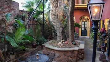 A courtyard with a brick wall, palm trees, a table with chairs, and a lantern.