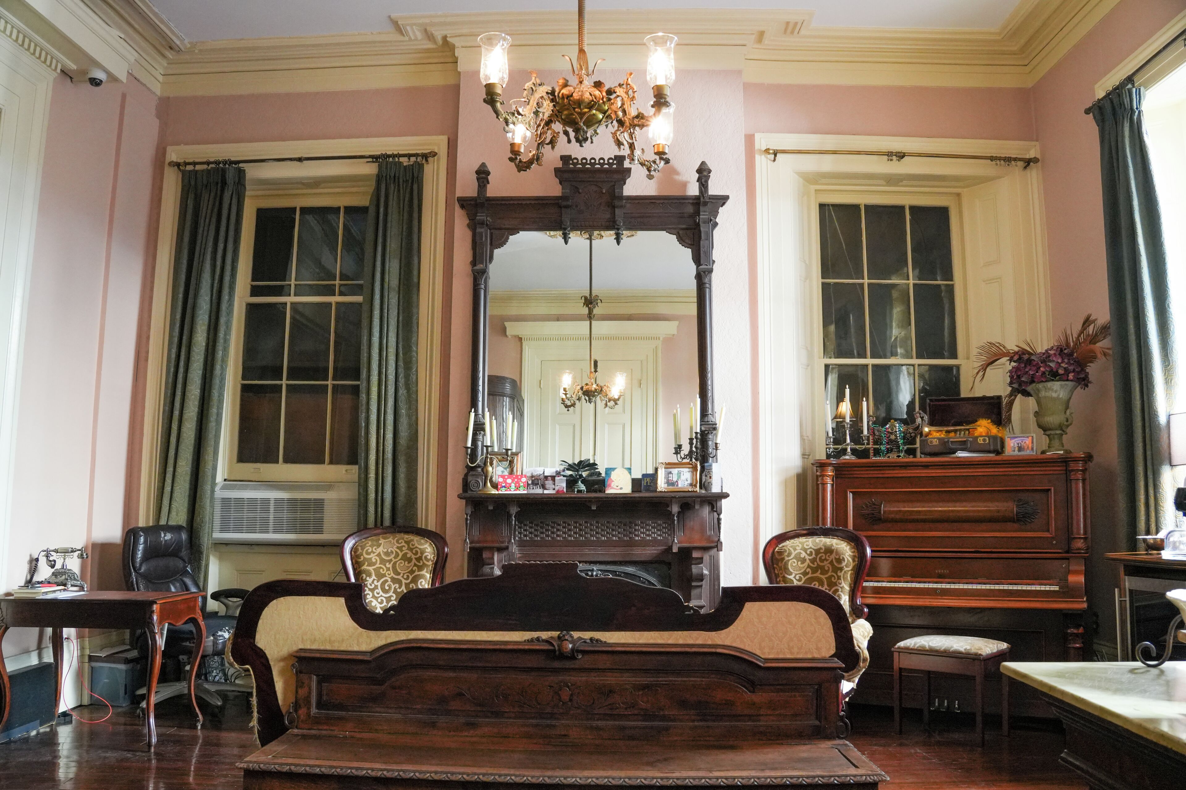 A room with a large mirror, a wooden bed, a piano, and a chandelier.