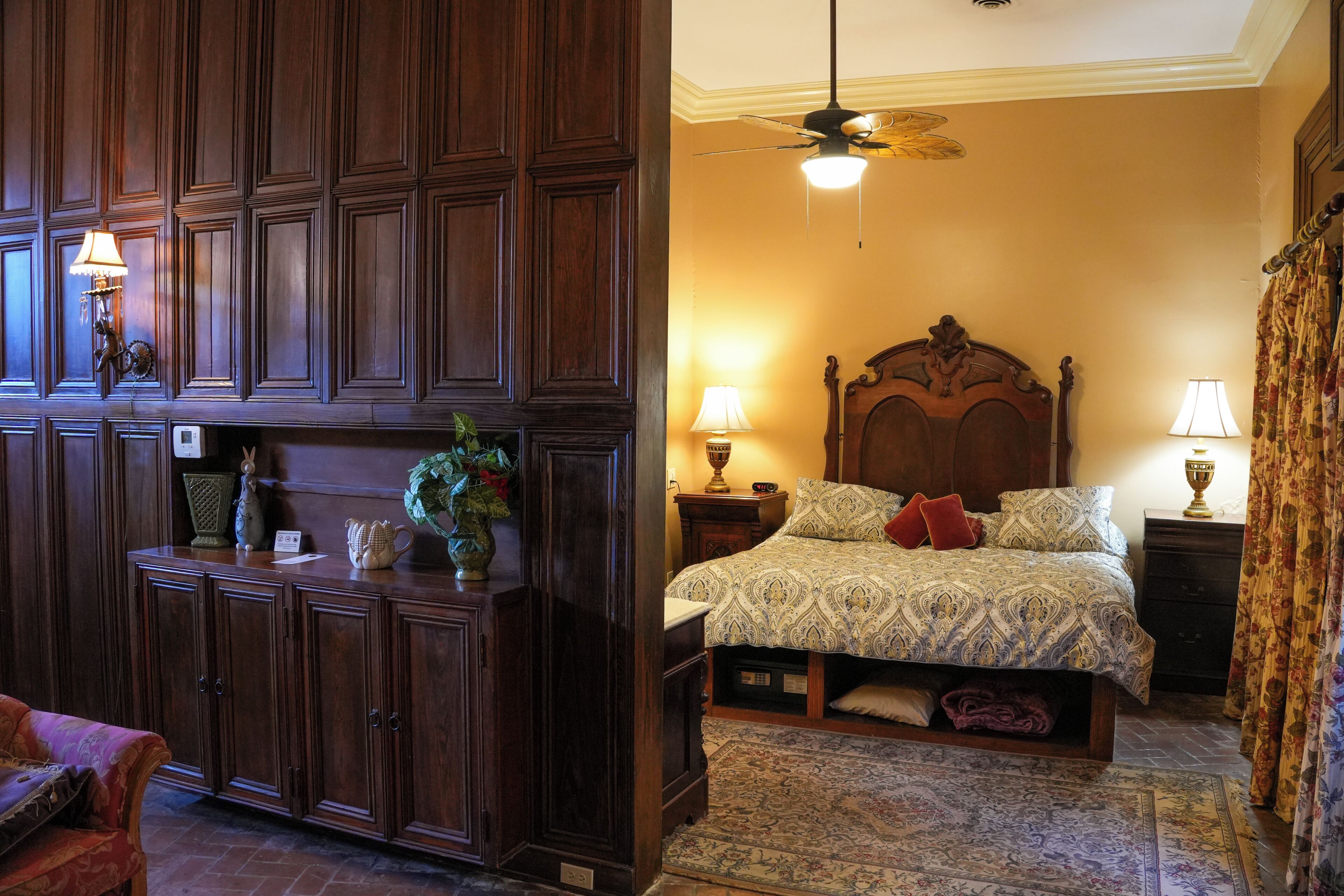 Una habitación con un armario de madera, una cama con ropa de cama estampada, un ventilador de techo y dos lámparas de noche.