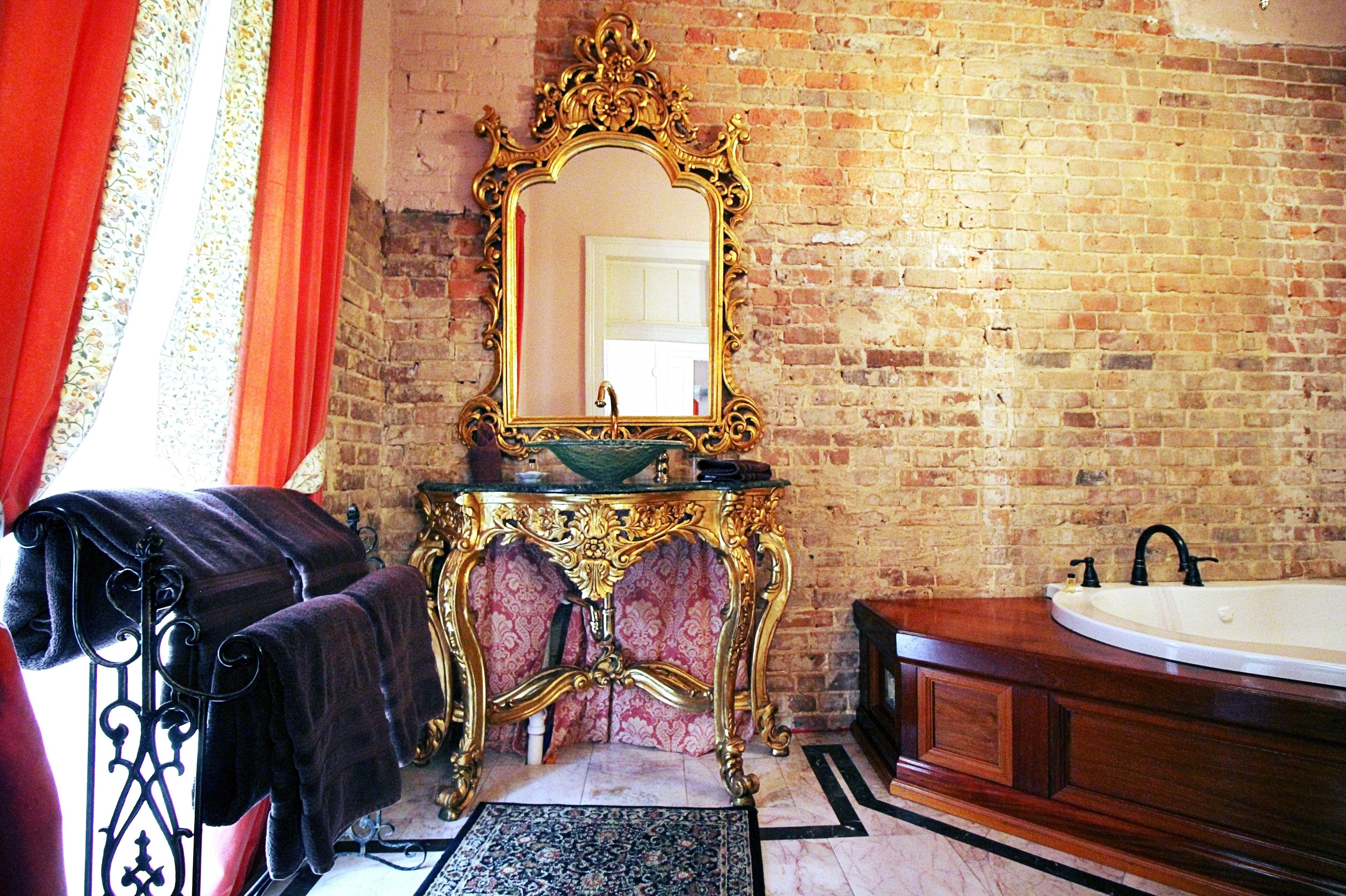 A bathroom with a brick wall, a gold-framed mirror, a sink, and a bathtub.