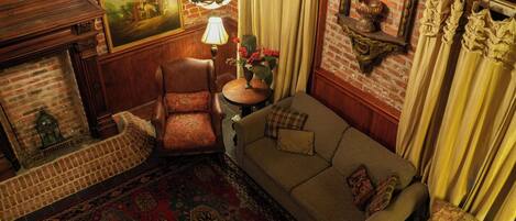 A room with a brick wall, a wooden sofa, a patterned rug, a wooden chair, a table with a vase, and a chandelier.